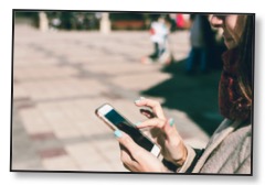 Picture of a woman outdoors scrolling on a mobile phone communicating the ease of global consumption and disconnection. 