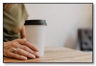 Picture of a woman's hand next to a hot take away drink on a table, communicating support is available for dementia. 