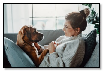 Picture of a woman reclining on a couch with a dog on her lap looking at each other in a supportive relationship.