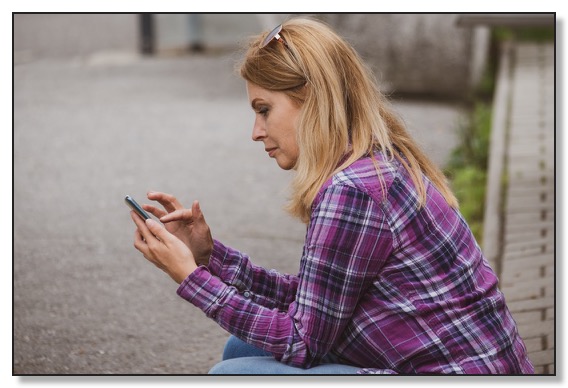 Picture of a woman sitting outside scrolling on a mobile phone, looking lonely and needing help to have healthy relationships.