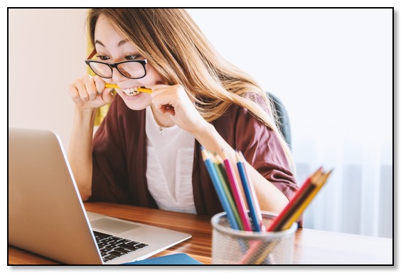 Picture of a woman looking intently at a laptop while biting on a pencil, communicating that with support healthy relationships are possible.