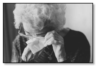 Black and white picture of a woman wearing glasses wiping tears from her eyes, sad at being alone and not having supportive relationships.