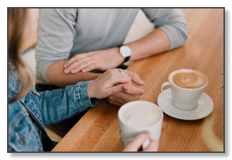 Picture of a couple at a table with hot drinks; one resting a comforting hand on top of the other, communicating the need for support in relationships when feeling alone.